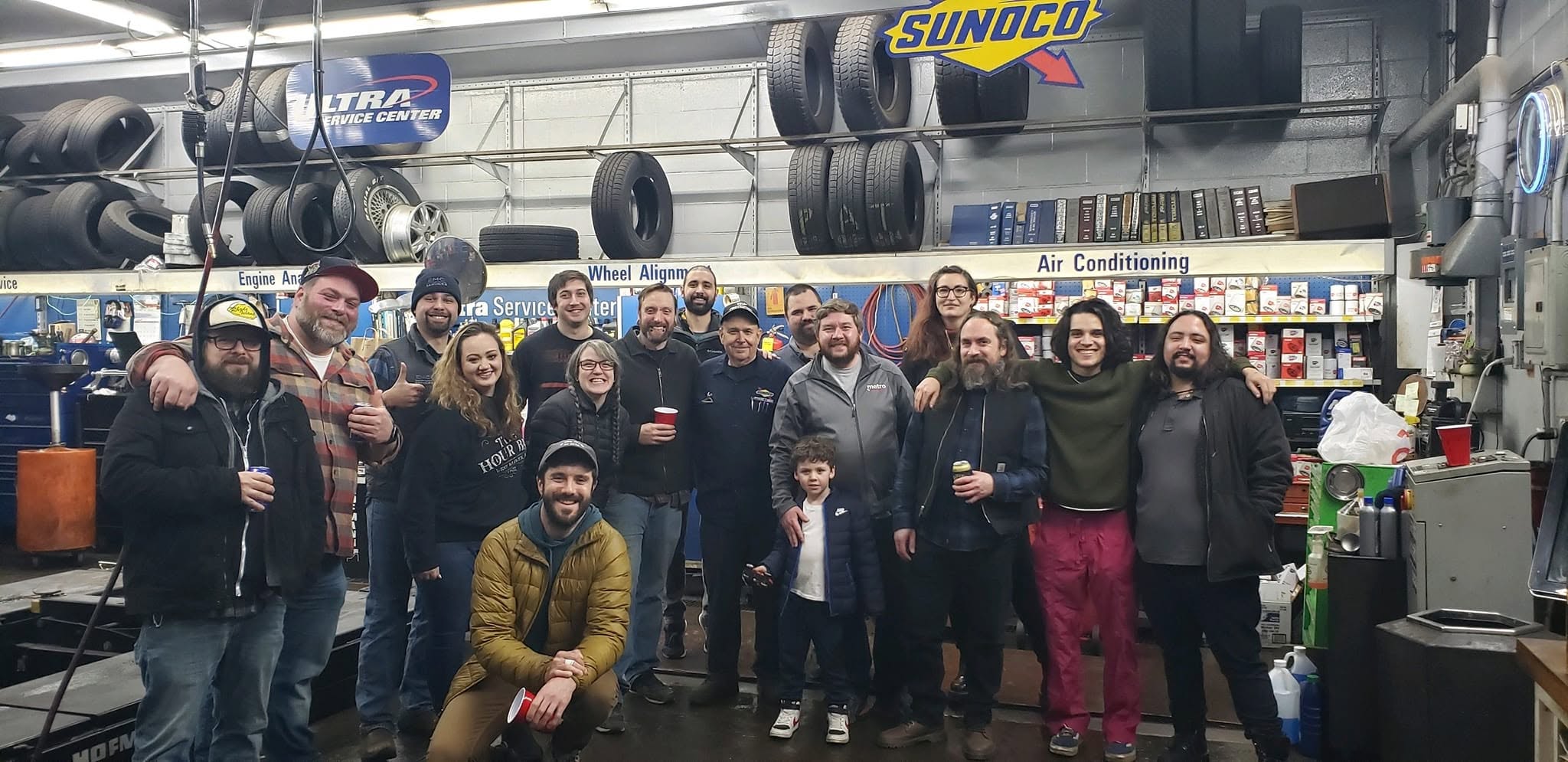 The Pawtuxet Auto Service team: a group photo of the whole crew inside the shop in front of the tire racks